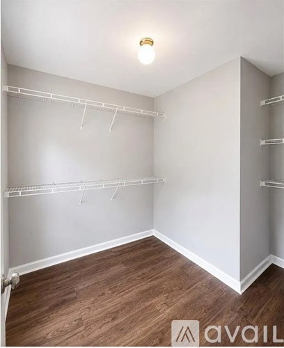 A room with white walls and wooden flooring, equipped with white shelving.