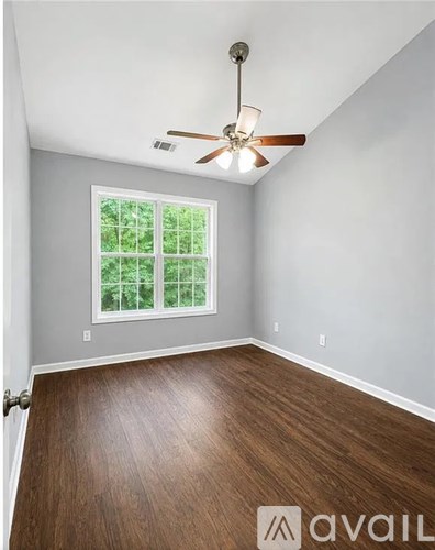 A room with a ceiling fan and a window with a view of trees.