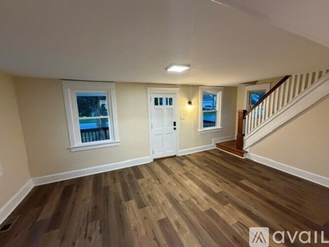 A room with wooden flooring and a staircase leading to another room.