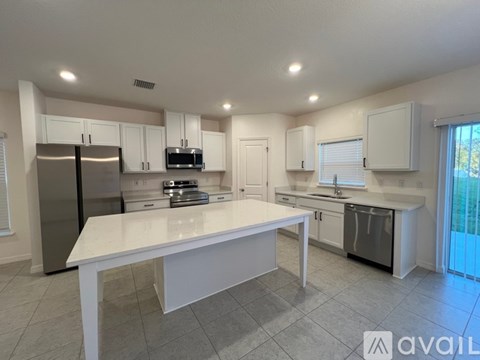 A kitchen with white cabinets and appliances, a large island in the center, and a sliding glass door leading to a balcony.