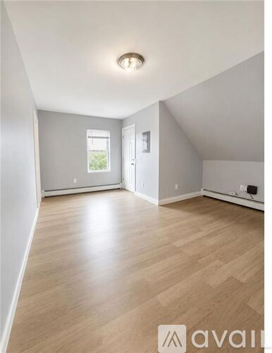A spacious room with wooden flooring and a window.
