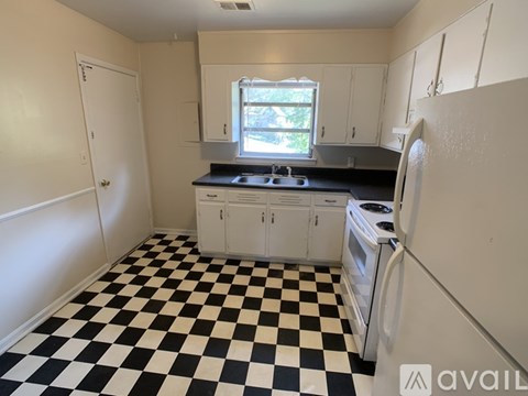 A black and white checkered floor in a kitchen with white cabinets and a window.