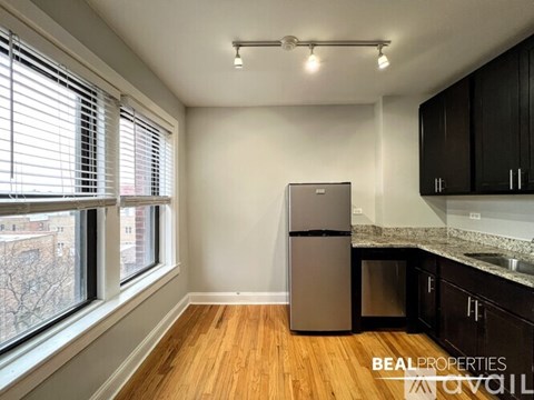 A kitchen with a refrigerator, cabinets, and a window with blinds.