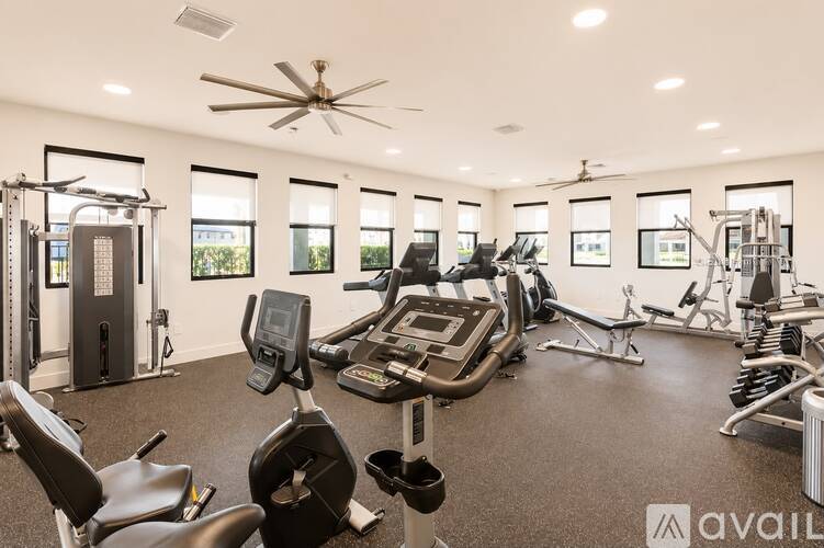 A well-equipped gym with various exercise machines and a ceiling fan.