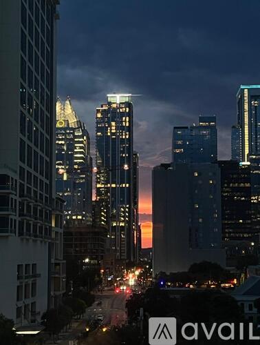A cityscape at dusk with tall buildings and a sunset in the background.