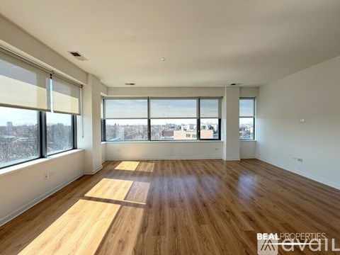 A spacious room with wooden flooring and large windows overlooking a cityscape.