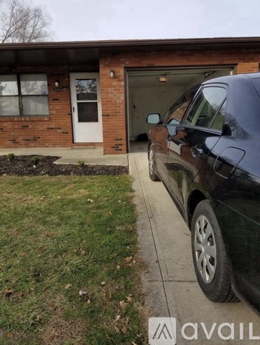 A black car is parked on the sidewalk in front of a brick house.