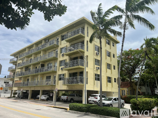A yellow apartment building with balconies and cars parked in front.