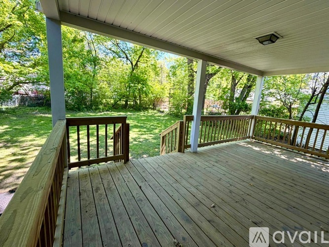 A wooden deck with a railing and a view of a green lawn and trees.