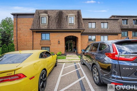 Two cars are parked in front of a brick house.
