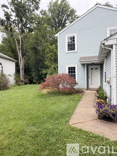 A blue house with a white door and windows is surrounded by greenery.
