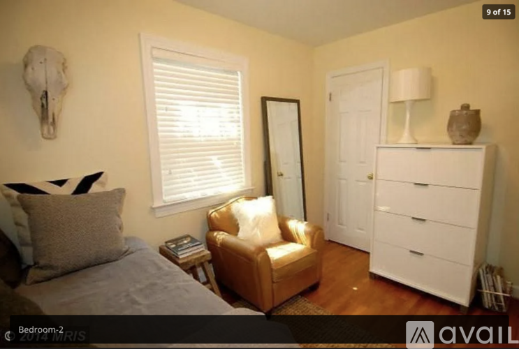 A bedroom with a bed, a chair, a skull decoration, a cabinet, and a window with blinds.