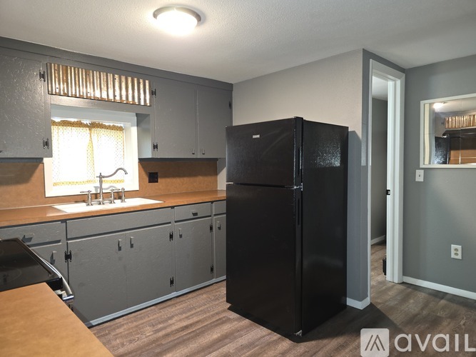 A black refrigerator in a kitchen with wooden flooring and grey cabinets.