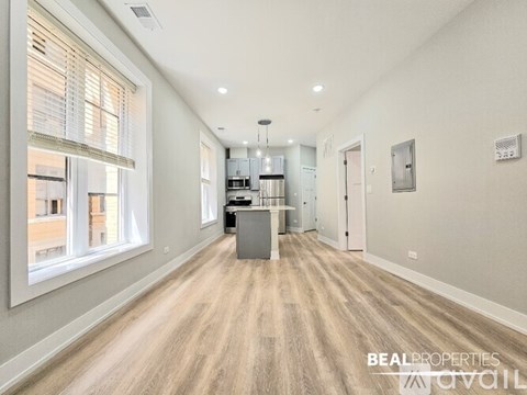A spacious, well-lit room with wooden flooring and a kitchen area in the background.