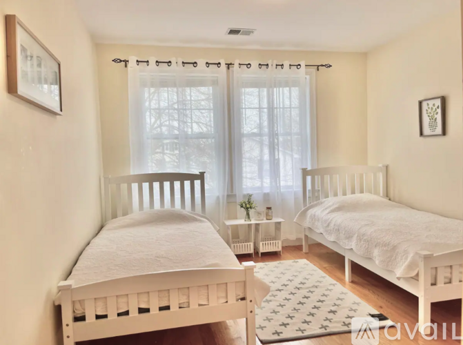 A white bedroom with two beds and a window with curtains.