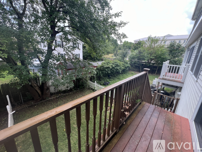 A wooden deck overlooks a backyard with a white house and trees.