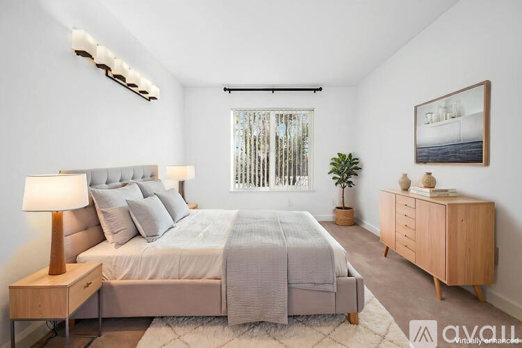 A well-lit bedroom with a large bed, a nightstand, and a wooden dresser.