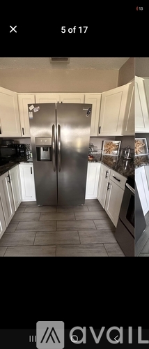 A kitchen with a stainless steel refrigerator and black countertops.