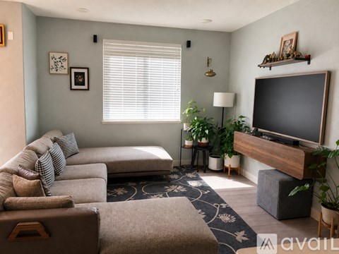 A living room with a grey couch, a brown leather ottoman, a television, and a rug.