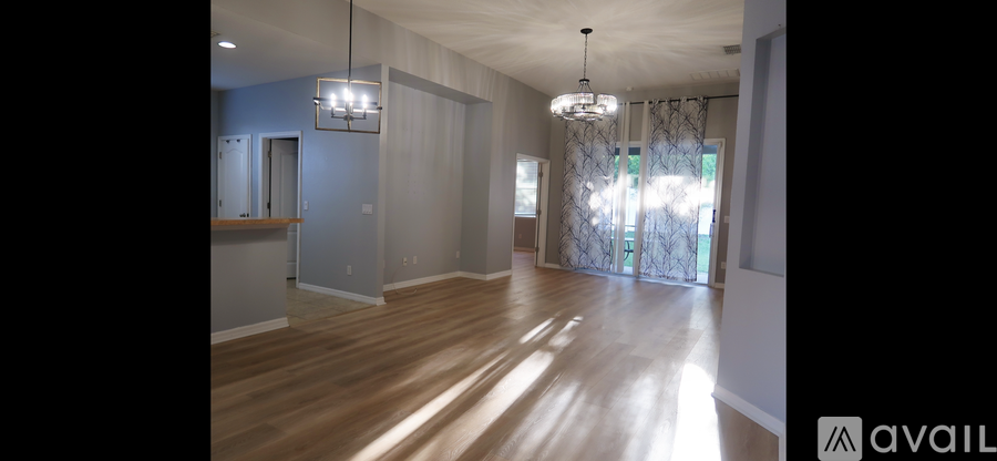 A spacious room with wooden floors and a large window with curtains.