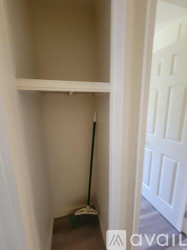 A broom is leaning against the wall in a white hallway.