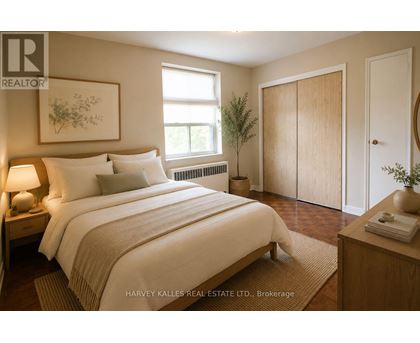 A bedroom with a large bed, a nightstand with a lamp, a window with a view of the sky, a plant, and a door.