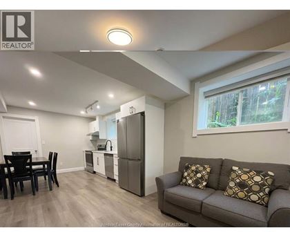 A well-lit living room with a grey couch and a kitchen area in the background.