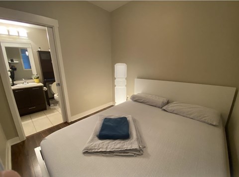 A bed with a white comforter and a blue pillow case is in a room with a mirror and a lamp.