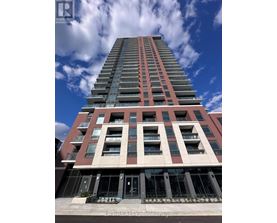 A tall building with a red and beige facade stands under a blue sky with clouds.