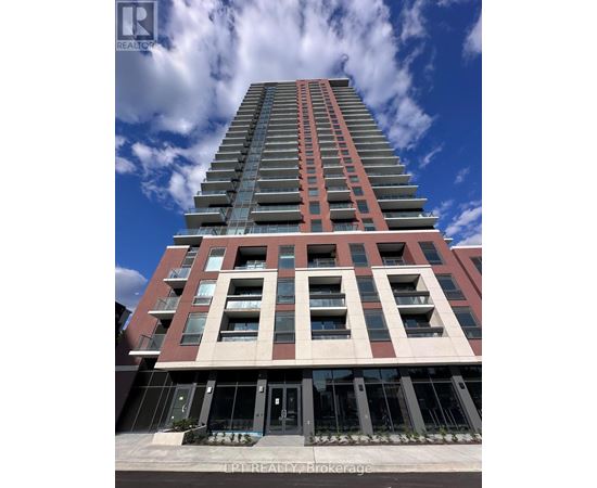 A tall building with a red and beige facade stands under a blue sky with clouds.