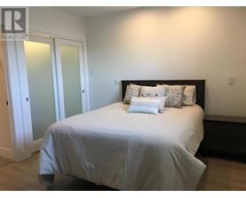 A bed with a white comforter and two pillows sits in a bedroom with a white door and a black headboard.