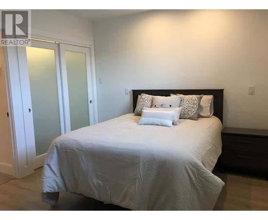 A bed with a white comforter and two pillows sits in a bedroom with a white door and a black headboard.