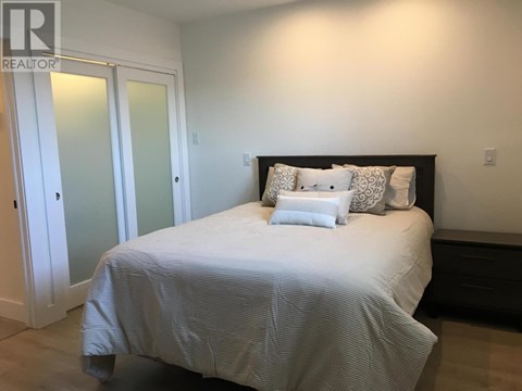 A bed with a white comforter and two pillows sits in a bedroom with a white door and a black headboard.