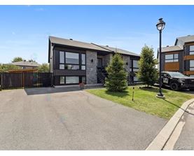 A modern house with a grey driveway and a black car parked in front.