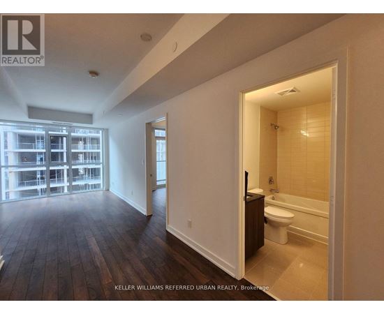 A spacious room with a wooden floor and a bathroom visible through the door.