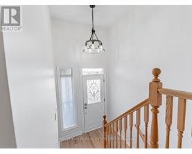 A white hallway with a wooden staircase and a chandelier.
