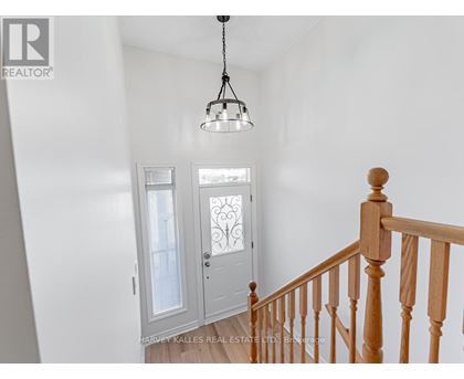 A white hallway with a wooden staircase and a chandelier.