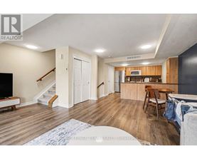 A living room with a staircase and a kitchen area in the background.