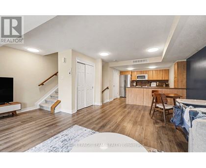 A living room with a staircase and a kitchen area in the background.