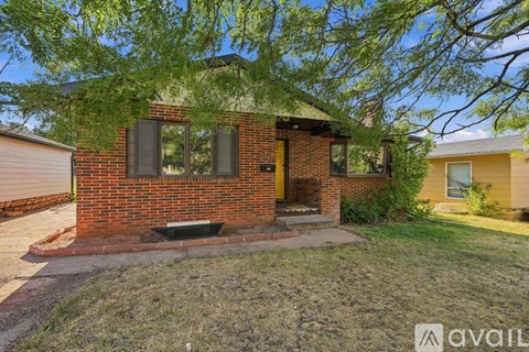 A house with a red brick exterior and a yellow door is surrounded by a grassy area and trees.