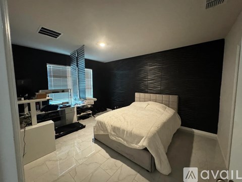 A bedroom with a bed, desk, and window with blinds.