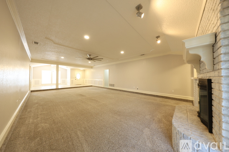 A spacious room with a carpeted floor and a fireplace on the right side.