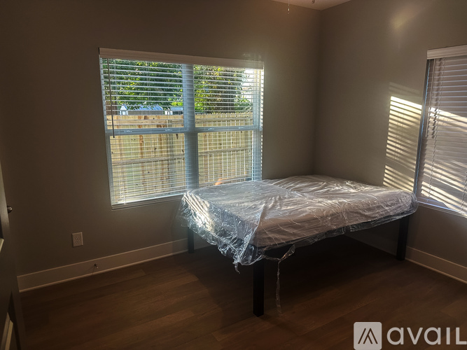 A bedroom with a bed covered in plastic and a window with blinds.