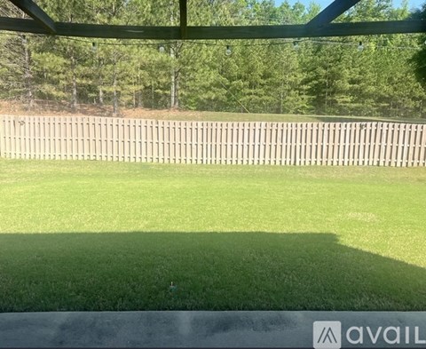 A grassy field with a wooden fence and trees in the distance.