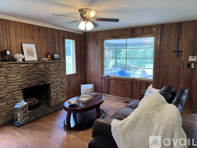 A living room with a stone fireplace and a ceiling fan.