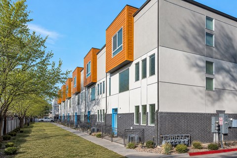 A row of modern townhouses with a sidewalk and greenery.