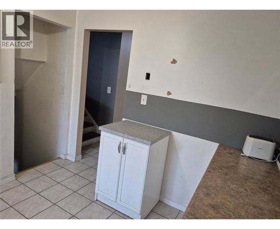 A white cabinet with a granite countertop is in a room with a grey wall and a door.