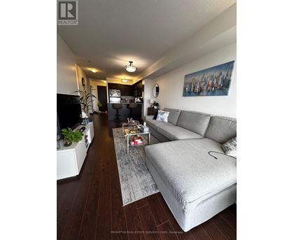 A living room with a grey couch and a painting on the wall.