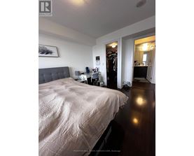 A bedroom with a large bed and a closet with clothes hanging.