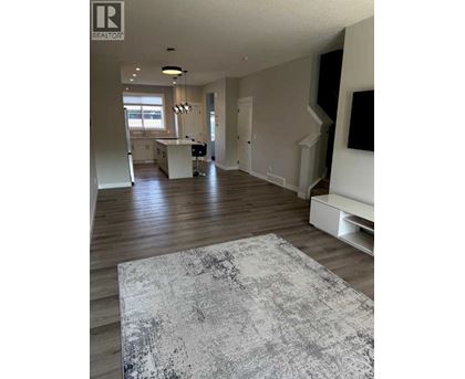 A large, open living room with a grey rug in the foreground and a kitchen area in the background.